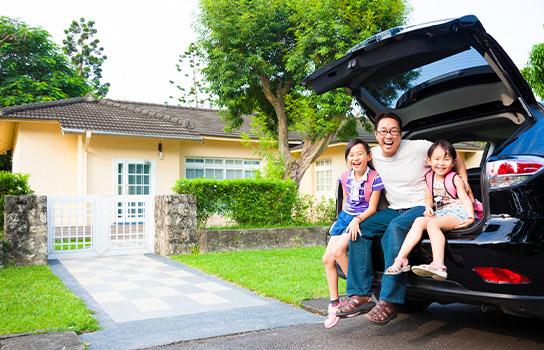 Dad and daughters sitting in the open trunk of a car outside home